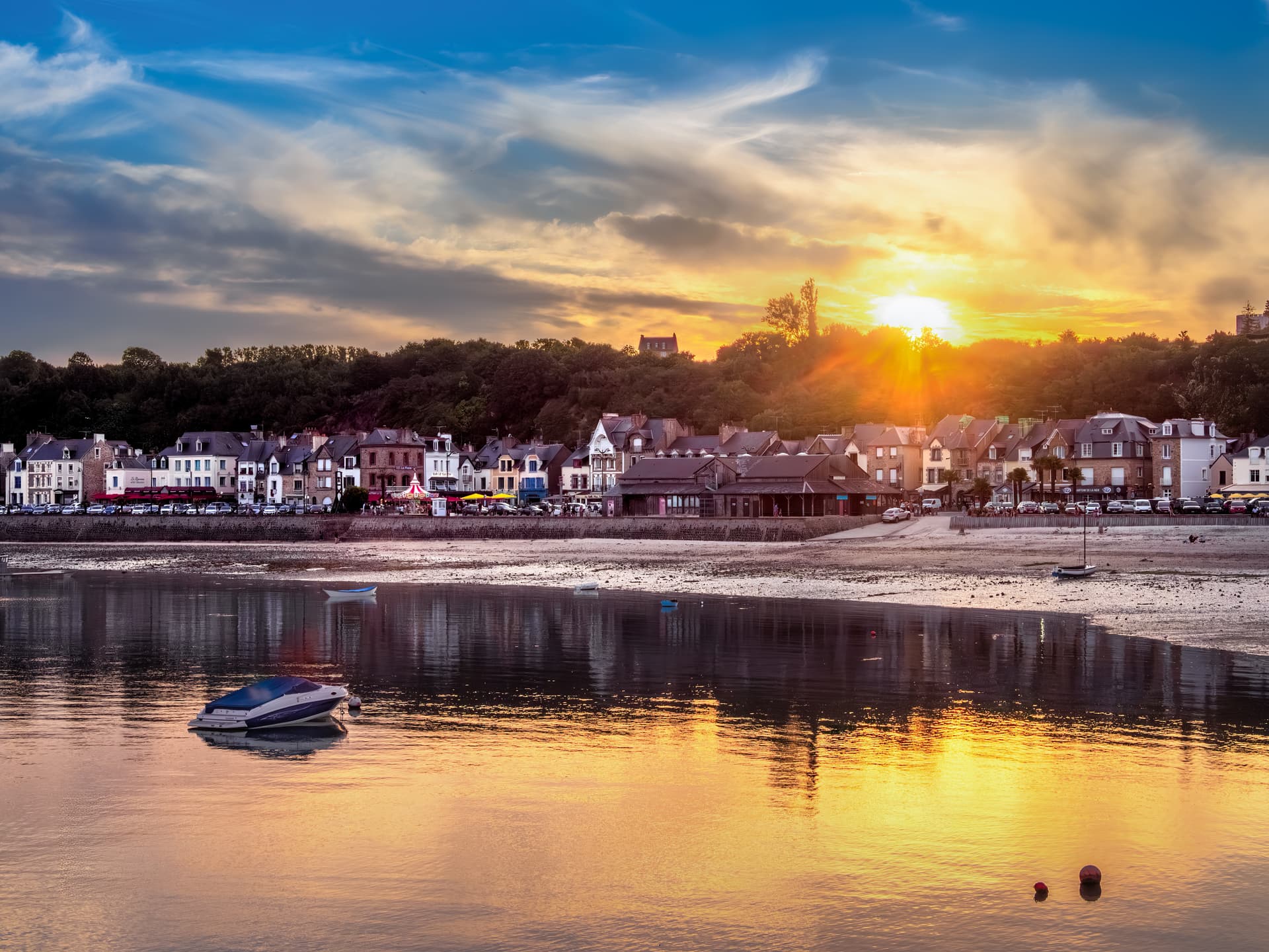 Serene coastal village of Cancale, Brittany, at sunset with low tide and boats on water.