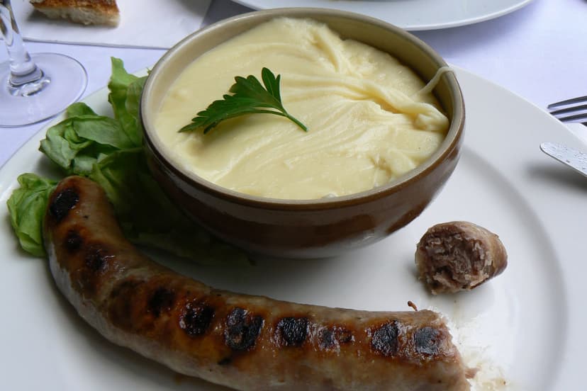 Aligot in a ceramic bowl with grilled sausage and lettuce on a white plate