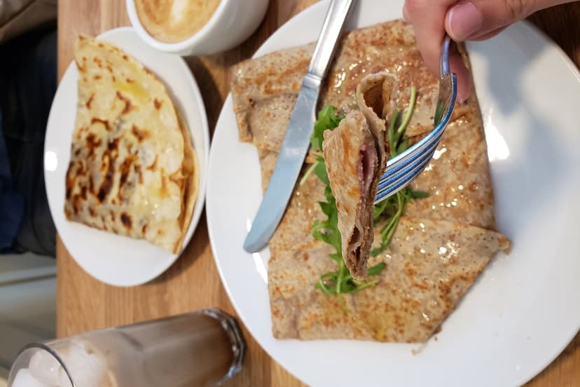 Buckwheat galette being eaten with a fork on a plate with greens