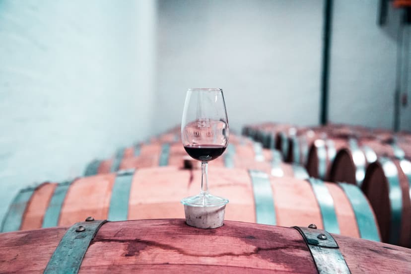 Glass of red wine resting on a wooden wine barrel in a cellar