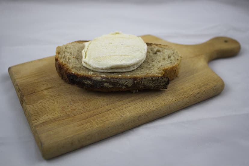 Rocamadour cheese on a slice of bread on a wooden cutting board