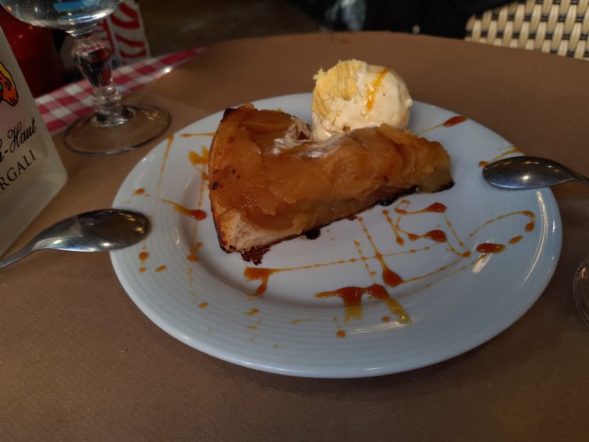 Tarte tatin slice with a scoop of ice cream on a white plate with caramel drizzle