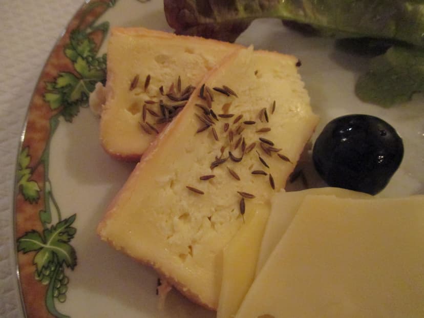 Munster cheese slices topped with cumin seeds on a decorative plate with lettuce and a dark olive